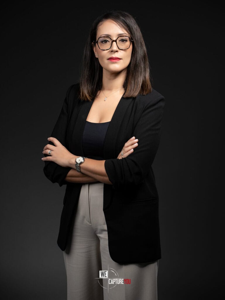 Confident woman in business attire with glasses against dark background.