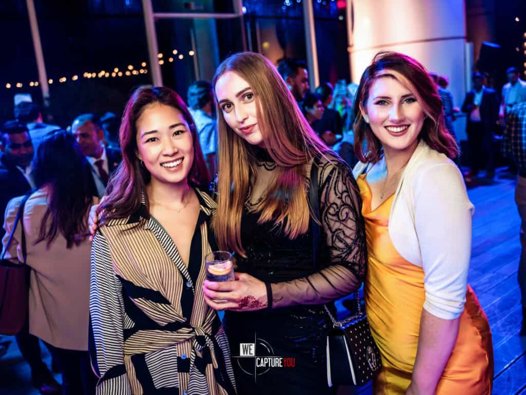 Three women smiling at Dubai event, vibrant party atmosphere.