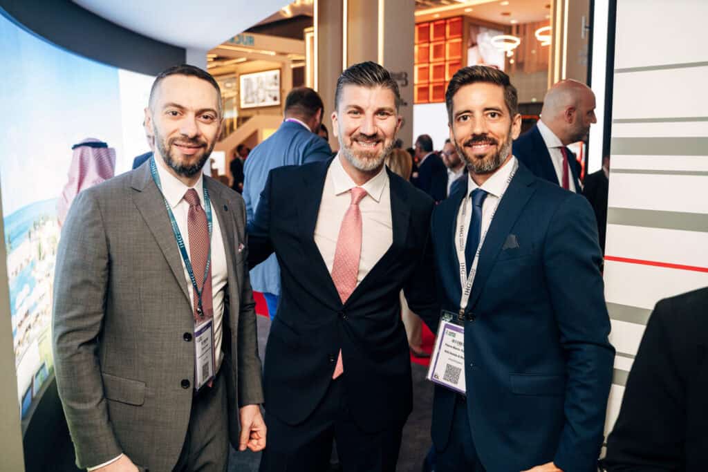 Three men in suits smiling at a professional event.