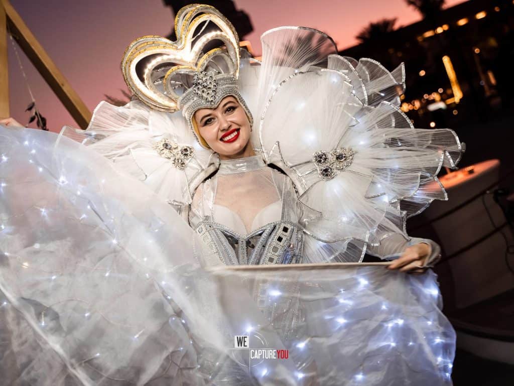 Elegant performer in white costume with heart-shaped headpiece at Dubai event.