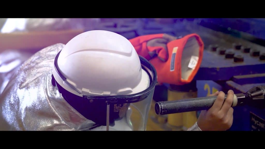 Worker wearing safety helmet and gloves operating machinery in industrial setting.