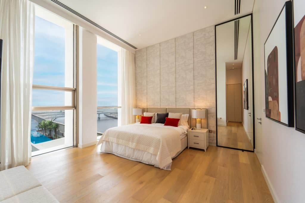 Modern bedroom with large windows and ocean view, minimalist decor, and wooden flooring.