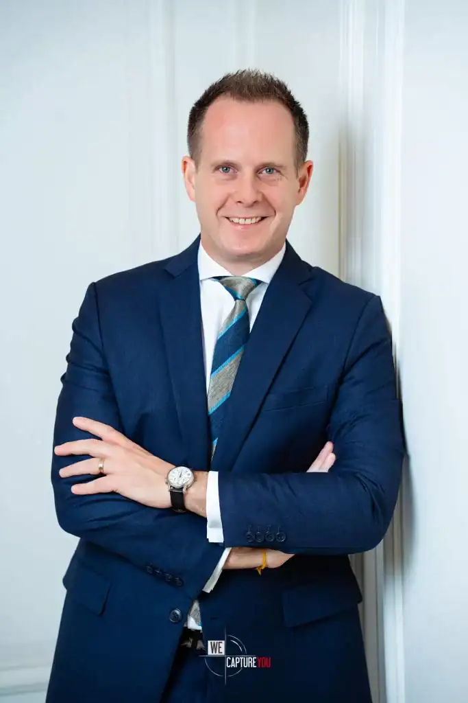 Confident businessman in blue suit smiling with arms crossed in office setting.