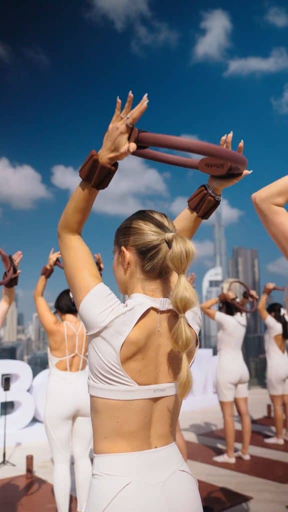 Women practicing yoga outdoors during Dubai event with city skyline in background.