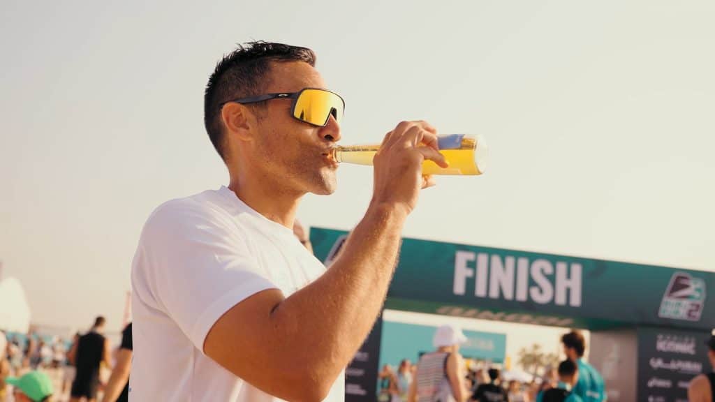 Man drinking energy drink at marathon finish line during sunset.